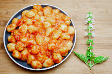 Traditional homemade Italian gnocchi in aromatic tomato sauce served on a decorative plate and garnished with herbs, basil, colored pepper, garlic and pink Himalayan salt. 