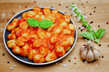 Traditional homemade Italian gnocchi in aromatic tomato sauce served on a decorative plate and garnished with herbs, basil, colored pepper, garlic and pink Himalayan salt. 
