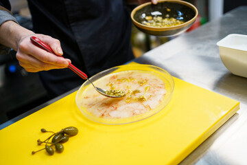 Anonymous cook spreading pine nut sauce on a plate of prawn carpaccio