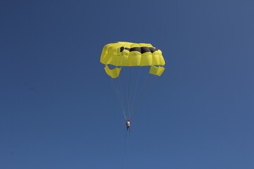 people flying on a beautiful yellow parachute against the blue sky. parachuting, entertainment at sea
