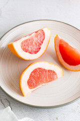 Ripe grapefruit slices on a plate on a light table. Sustainable food  lifestyle. Vertical view. Close-up
