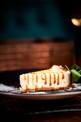 Piece of Cheesecake on black plate on a table with mint and a cup of coffee. Side view