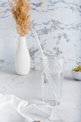 A glass of clean water and a glass straw for drinking on a light table. Diet organic lifestyle. Vertical view