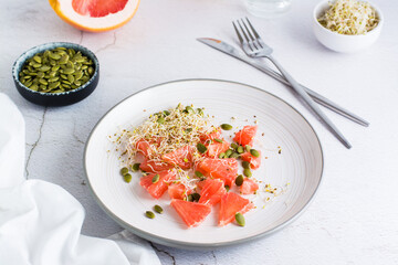 Fresh salad of grapefruit, clover and alfalfa sprouts and pumpkin seeds and cutlery on a plate on the table. Organic vegetarian detox food