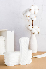 Clean disposable sanitary pads in a stack and in a box and a branch of cotton on a beige background. Women's health and comfort concept. Vertical view