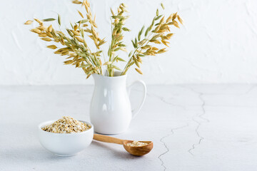 Dry oatmeal in a bowl and in a wooden spoon and a jug with ears on a light table. Home healthy food