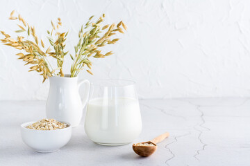 Oat milk in a glass, oatmeal in a bowl and ears in a jug on a light table. Alternative plant food