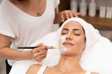 Aesthetics applying a mask to the face of a Middle-aged woman in modern wellness center.