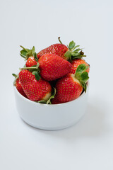 Close up of red juicy strawberries with green leaves in plate on white table. Healthy food concept. Gardening and harvesting at farm. Seasonable berries. Selective focus. 