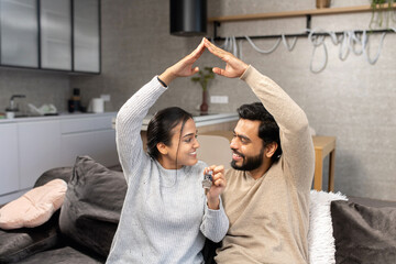 Happy Indian family couple showing new house keys to camera while posing Indoors. Own home, real estate ownership and housing. Mortgage and apartment purchase