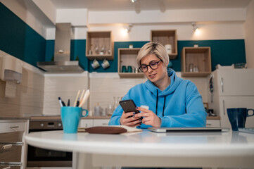 Short haired woman using smartphone in the kitchen at home