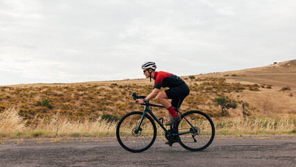 Side view of young woman cyclist riding on bicycle against hill - obrazy, fototapety, plakaty