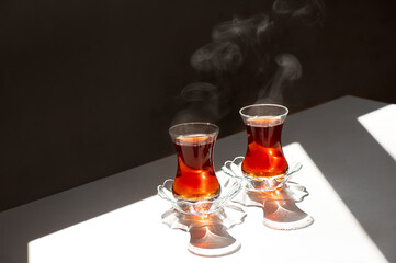 Close up of two traditional Turkish tea cup on white table in sunlight with steaming vapors at...