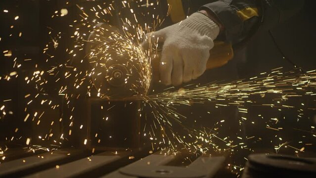 Industrial worker using an angle grinder and cutting a metal square pipe. Locksmith in special clothes in production. Industry machinery plant interior. Manufacturing metal structures. Close up, 4K