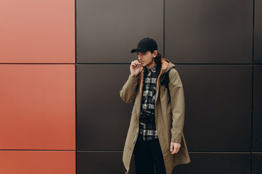 young handsome bearded hipster man smoking cigarette near wall on the street