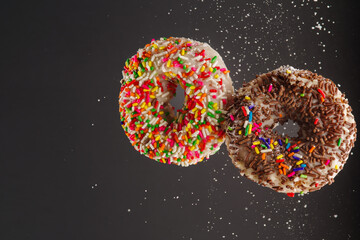 Two colored donuts and grains of powdered sugar in a frozen flight on a gray background. Holiday, sweet food, gourmet food. Shop, confectionery, cafe, restaurant, hotel.