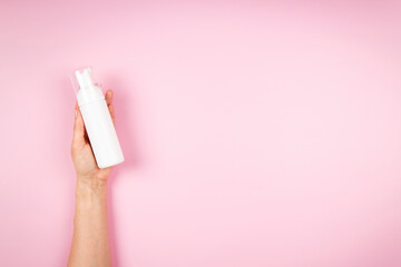Woman hands holding cosmetic mousse foam bottle on pastel pink background. Blank plastic package...