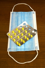 A half-empty blister with yellow tablets on a blue gauze mask on a wooden table for treatment and health, vertical format