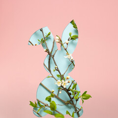 Pastel pink minimal concept with spring blossoming out of Easter bunny silhouette. Natural white flowers blooming on tree branches with bright green leaves.