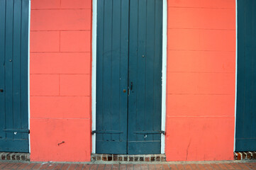 Green doors contrast with the dark pink walls on a home exterior in the French Quarter of New Orleans