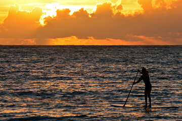 A young woman paddles towards the sunrise on Oahu, Hawaii's East Coast