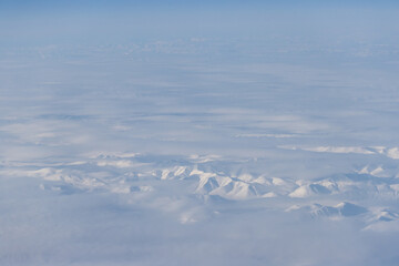 Aerial view of snow-capped mountains and clouds. Winter snowy mountain landscape. Kolyma Mountains on the border of Kamchatka Territory and Magadan Region, Siberia, Far East Russia. Great background.