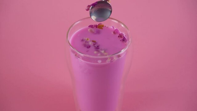 Pink rose milk. Mixing milk with rose petals with a spoon. Glass of moon milk.