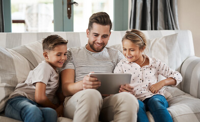 The go to gadget for learning time. Shot of an adorable little girl and boy using a digital tablet with their father on the sofa at home.