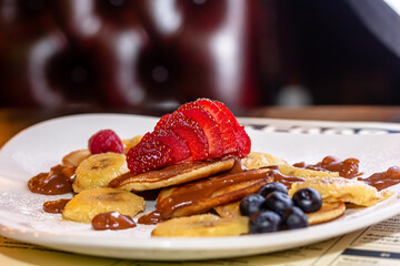 Pancakes with bananas, strawberries and blueberries are on a plate