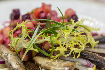 Sprat or sardines with salad vinaigrette are on a plate.
