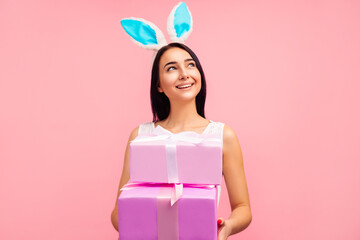Happy woman in rabbit ears with gifts in her hands, traditional holiday, in the studio on a pink...