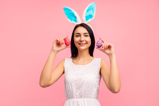 Beautiful and positive brunette woman in bunny ears and with painted Easter eggs pared eyes, easter