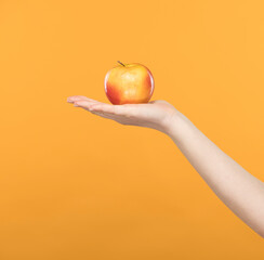 a pink-yellow apple lies on an open female palm on a yellow background close-up