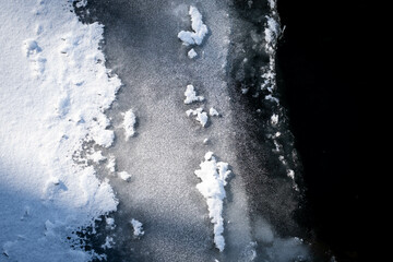 Frozen rivers edge showing a progression of snow covered land to flowing unfrozen water in a dramatic pattern