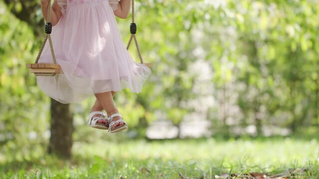 Spring and happy summer time. Closeup of feet of joyful little girl swinging on the swing, child plays in the green sunny garden at home, concept of healthy growth