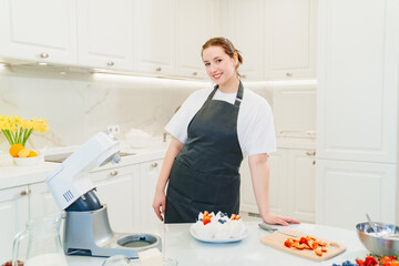 a young woman decorates cupcakes with white cream and fresh berries