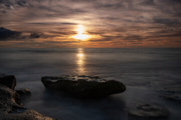 Fototapeta na wymiar rock in the middle of the sea at sunset or sunrise, calm and mysterious sea