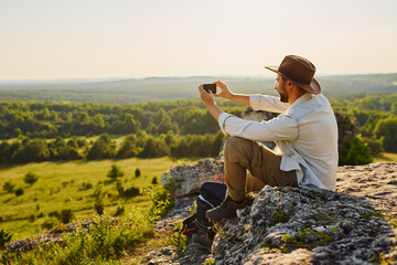 Male hiker sits on rocks taking picture with mobile phone. Jura, Poland.