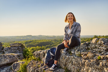 Naklejka na ściany i meble Happy woman hiker sitting on rock at top of the mountain enjoying summer hike