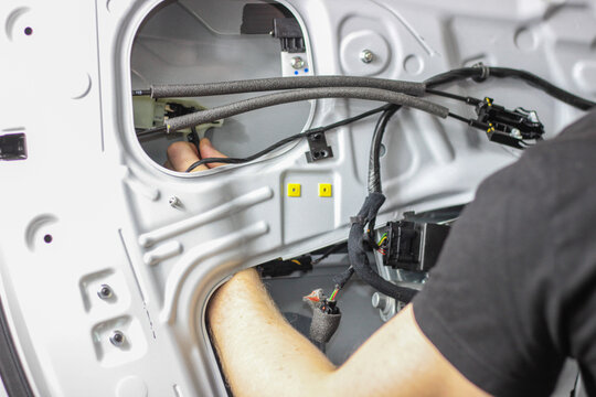 The man is concentrating on disassembling the car door to fix the electric window lifter. Repair of a car at a service station by a qualified employee. Finding a problem in a faulty car.