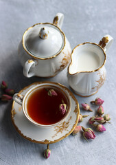 Tea with roses close up photo. Herbal tea in a small white ceramic cup on a table. Light grey background with copy space. 