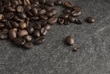 Brown aromatic roasted coffee beans on a gray stone background.