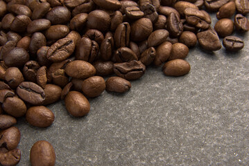 Brown aromatic roasted coffee beans on a gray stone background.