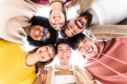 Multiracial group of friends standing in circle smiling at camera - Young people bonding and having fun outside - Millenial students hugging together support each other