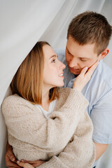 a happy and loving couple hugs against the background of a white curtain. 