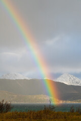 A beautiful rainbow over the ocean during sunset, with mountain ranges in the background