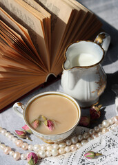 Simple composition still life with milk jug, cup of tea and an open book on a table. Close up photo of retro styled objects. Sunny day photo. 