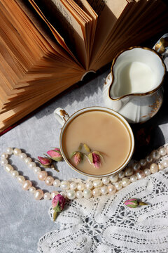 Cup of tea with milk and roses. Tea in beautiful vintage cup. Close up photo of hot aromatic beverage. 