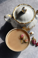 Obraz na płótnie Canvas Tea with roses close up photo. Herbal tea in a small white ceramic cup on a table. Light grey background with copy space. 