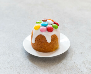 Festive Easter cake with icing sugar, decorated with colorful dragees, on a plate. Light grey background